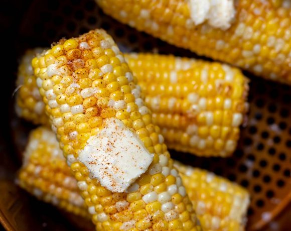 yellow corn on the cob topped with butter and spices, in air fryer basket
