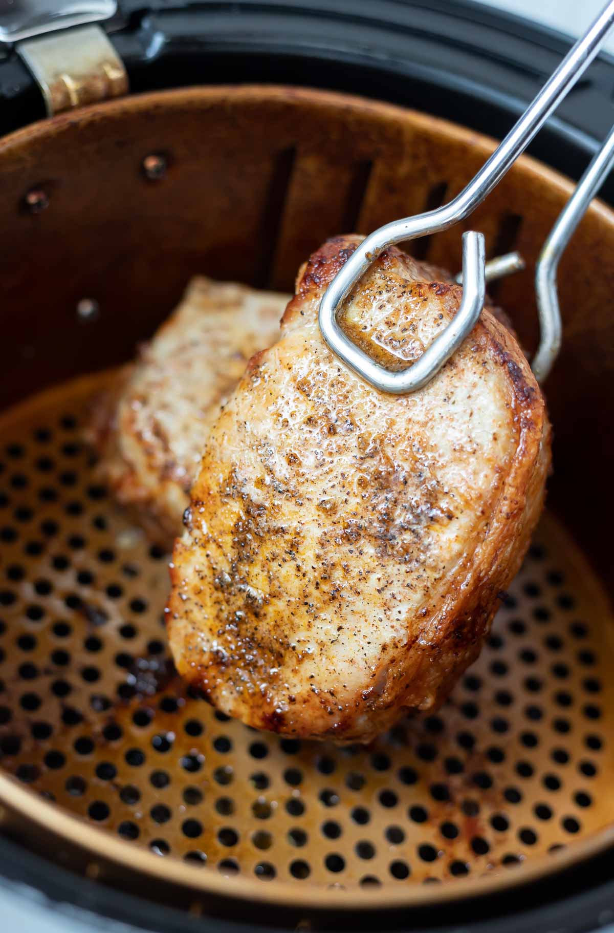 air fried pork chops being removed from air fryer with tongs