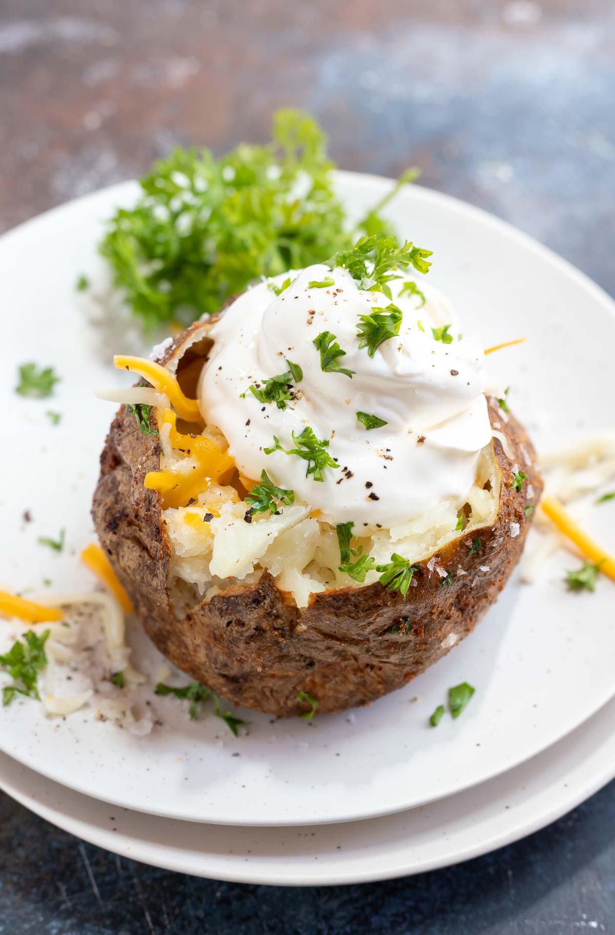 baked potato topped with sour cream and cheese served on white plate