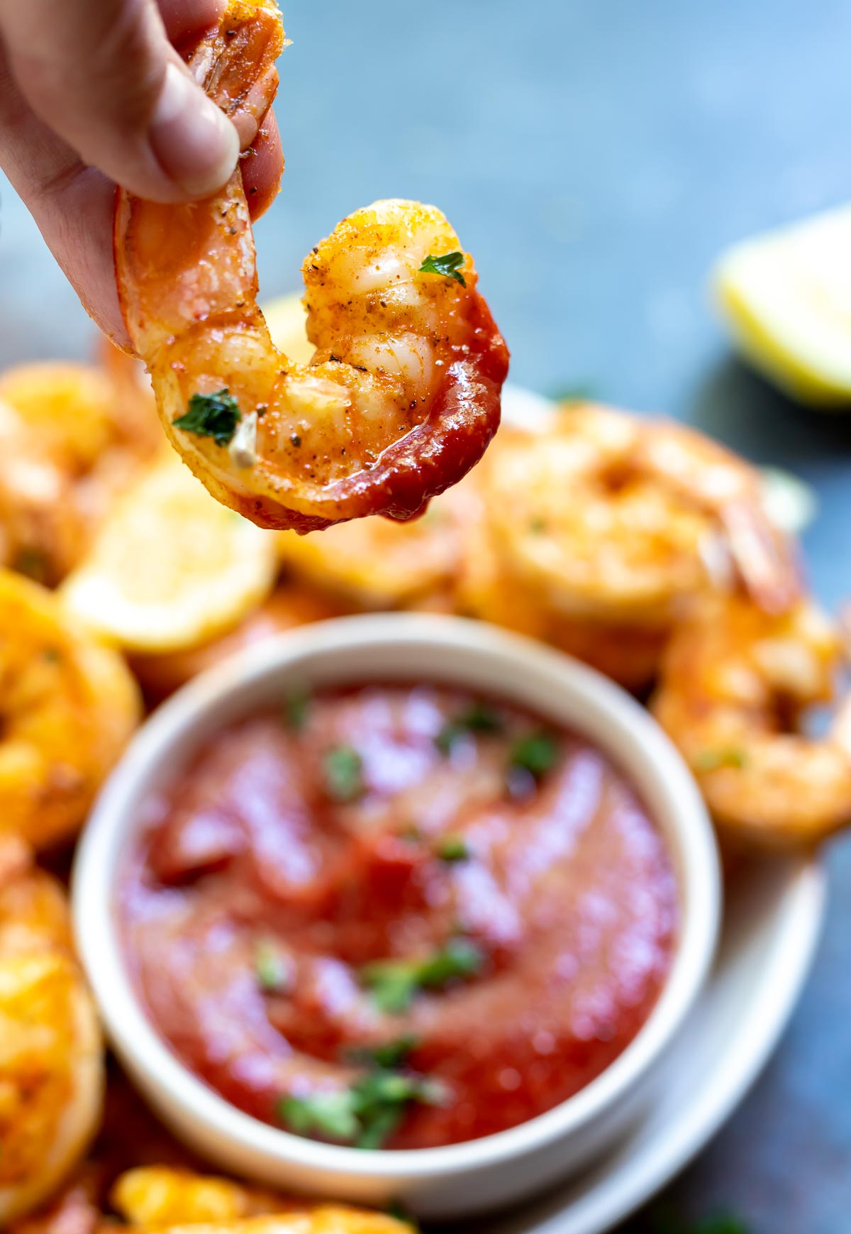 hand dipping air fried shrimp into cocktail sauce