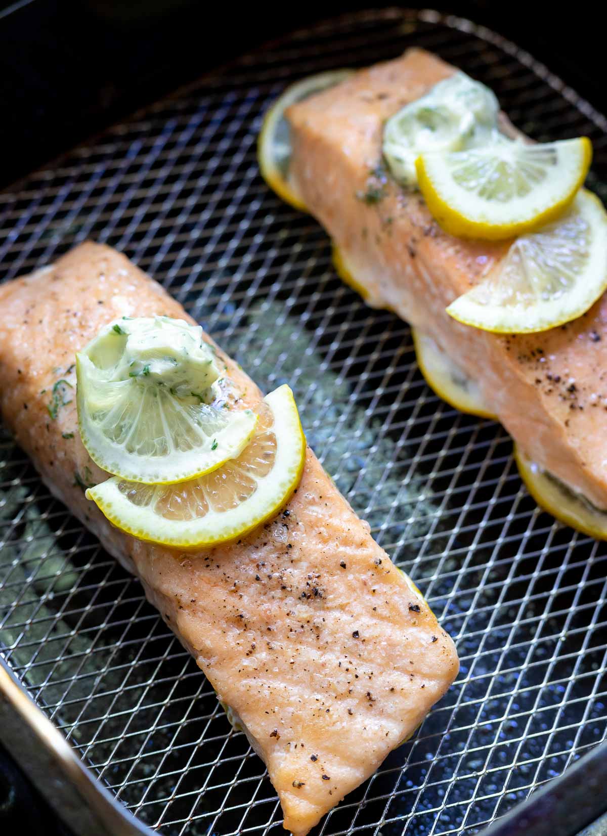 salmon fillets topped with butter and lemons in air fryer basket