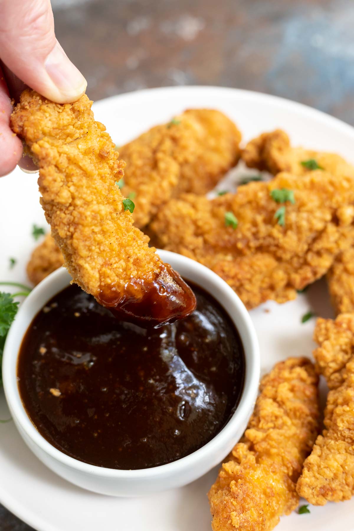 hand dipping air fried chicken strip into bbq sauce