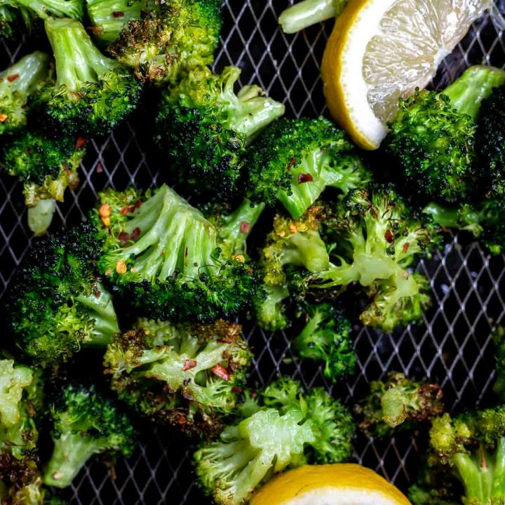air fried broccoli in air fryer basket with lemon wedges