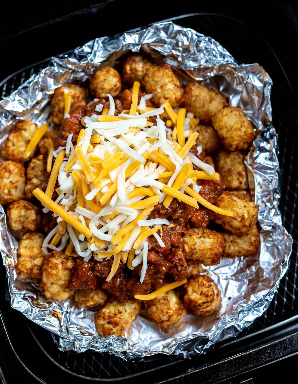 tater tots topped with chili and shredded cheese in air fryer basket