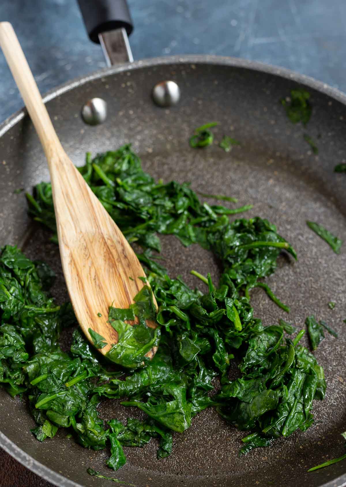 wilted spinach in pan with wooden spoon