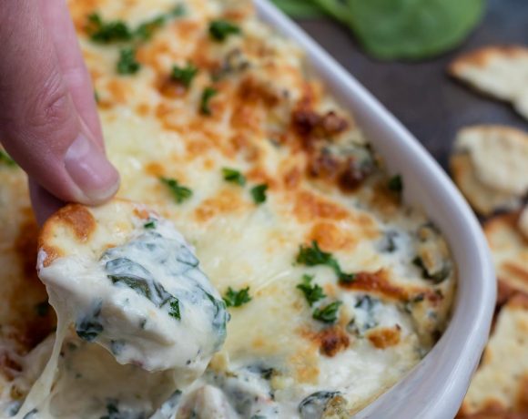 hand dipping cracker into hot spinach artichoke dip