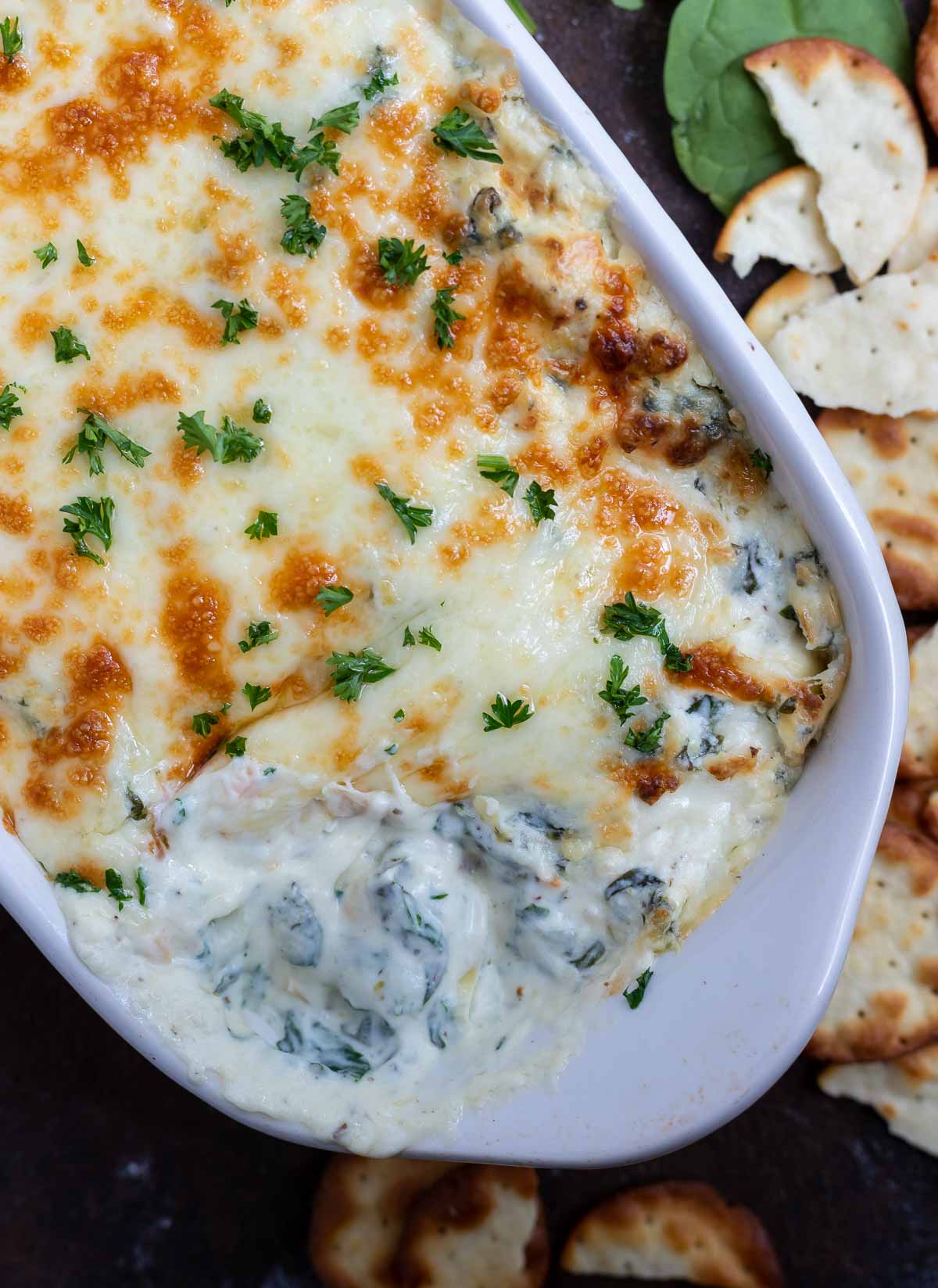 spinach artichoke dip in white dish surrounded by crackers
