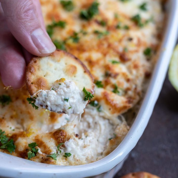 hand dipping cracker into crab dip