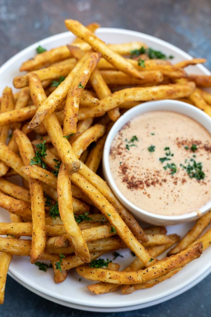 golden French fries on white plate with dipping sauce