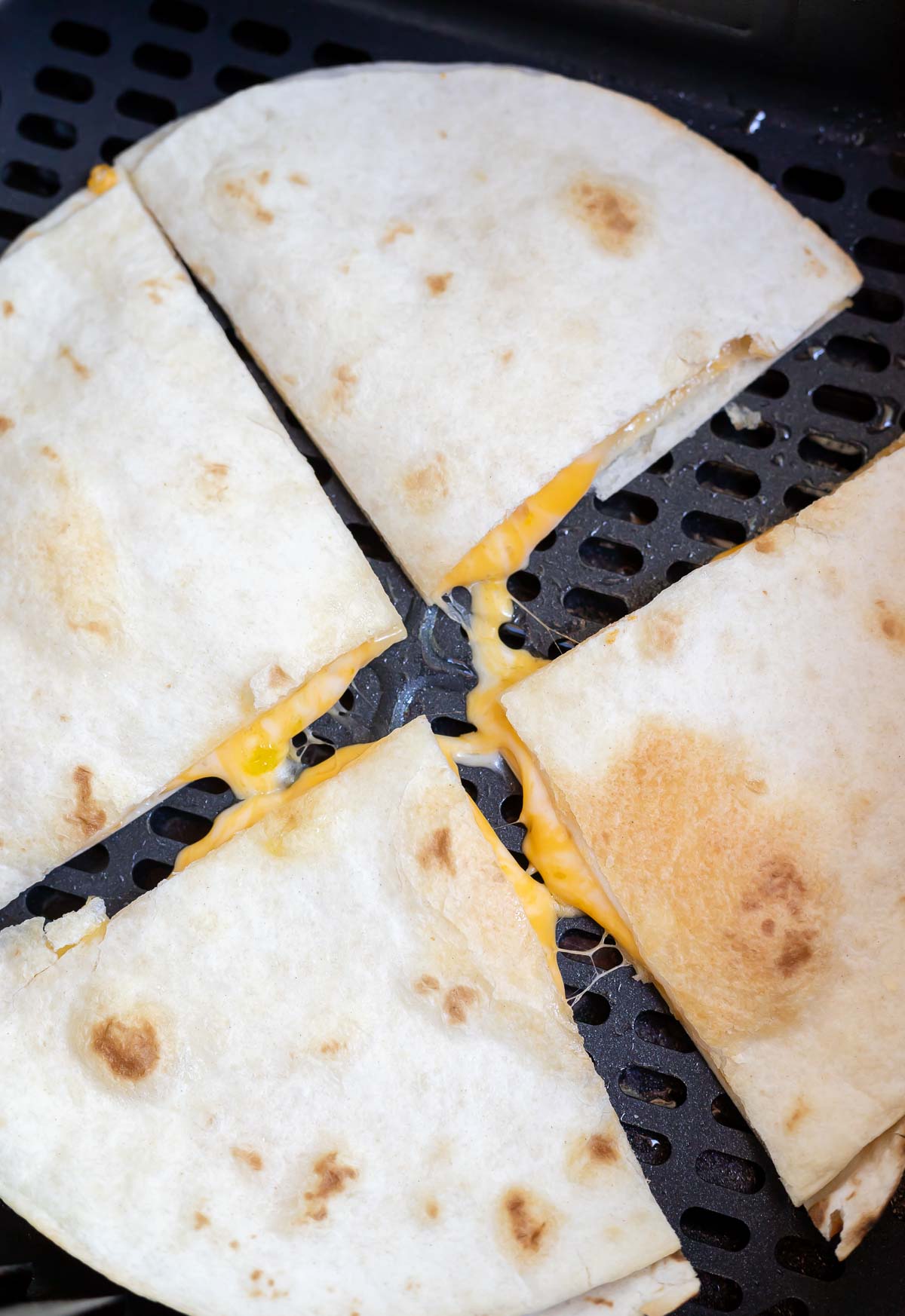 cooked quesadilla cut into four pieces in air fryer basket