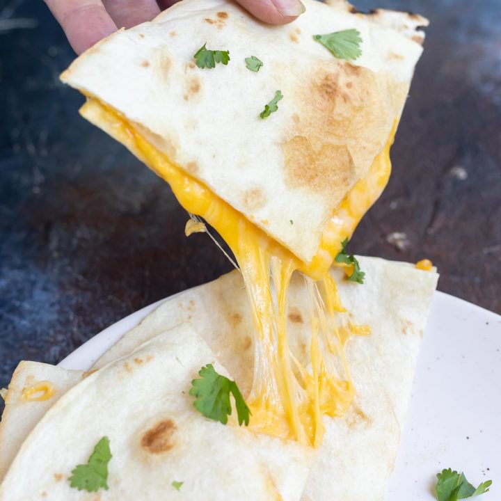 hand grabbing quesadilla wedge with melty cheese stretching