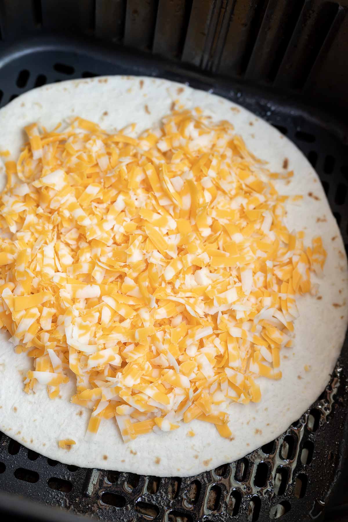 tortilla topped with shredded cheese in air fryer basket