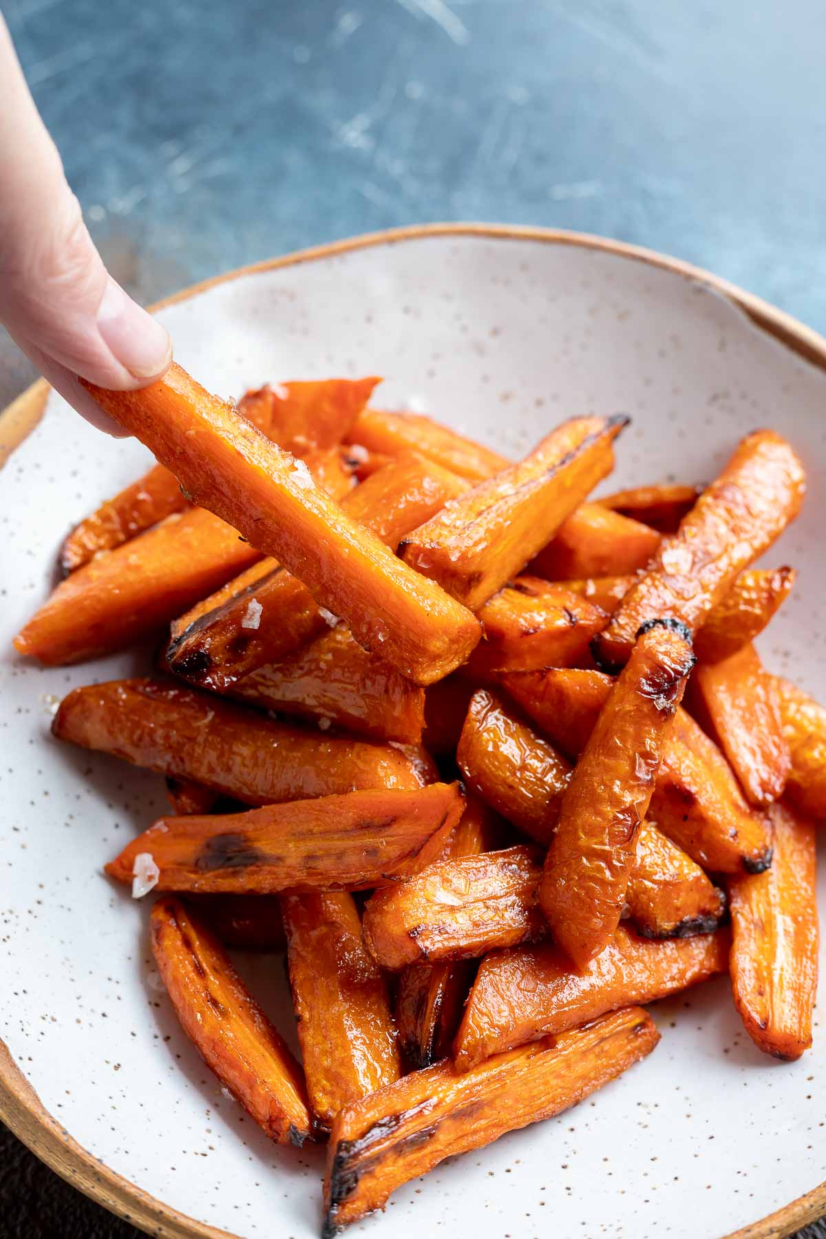 hand grabbing roasted carrot from white bowl