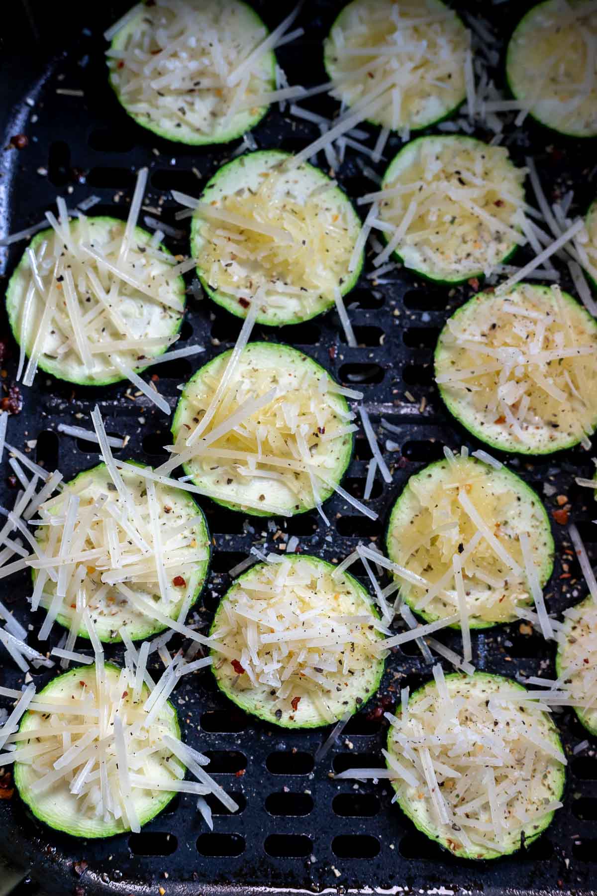 zucchini slices topped with shredded parmesan in air fryer basket
