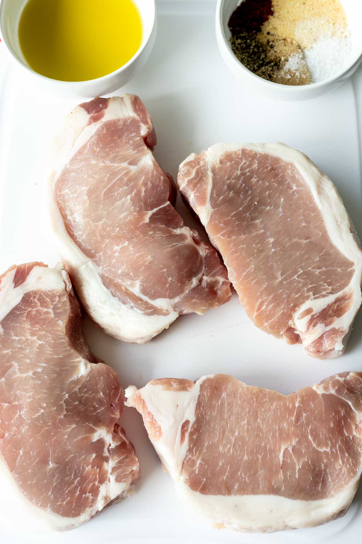 raw pork chops, oil and spice rub on cutting board