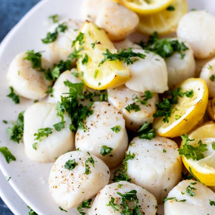 cooked scallops and lemons topped with chopped parsley served on white plate