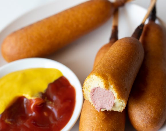 cooked corn dogs served on white plate with ketchup and mustard