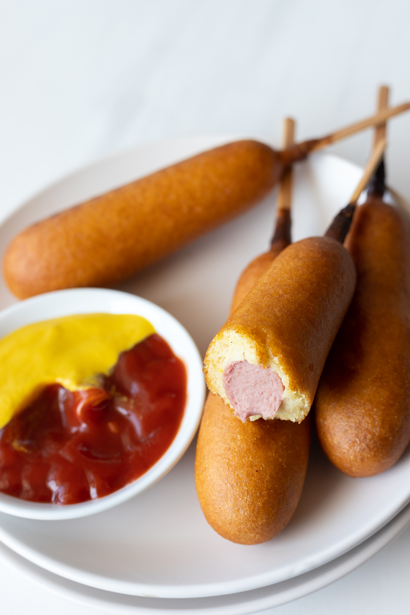 cooked corn dogs served on white plate with ketchup and mustard