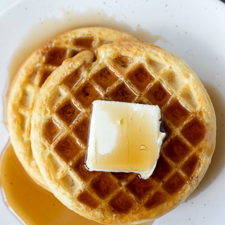 two cooked waffles with syrup and butter on white plate