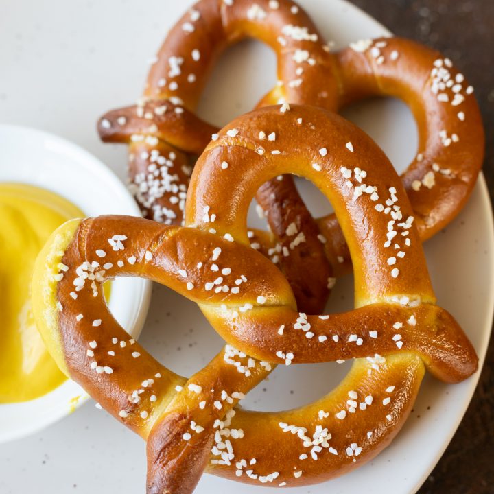 cooked pretzels on white plate next to yellow mustard