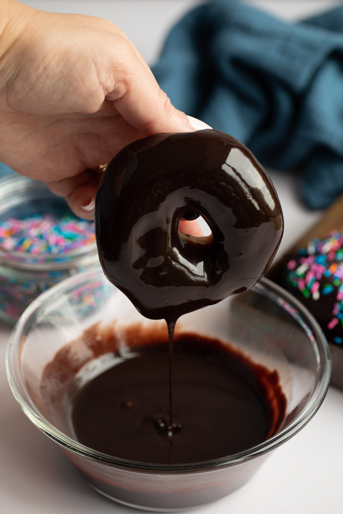 hand dipping donut into chocolate glaze