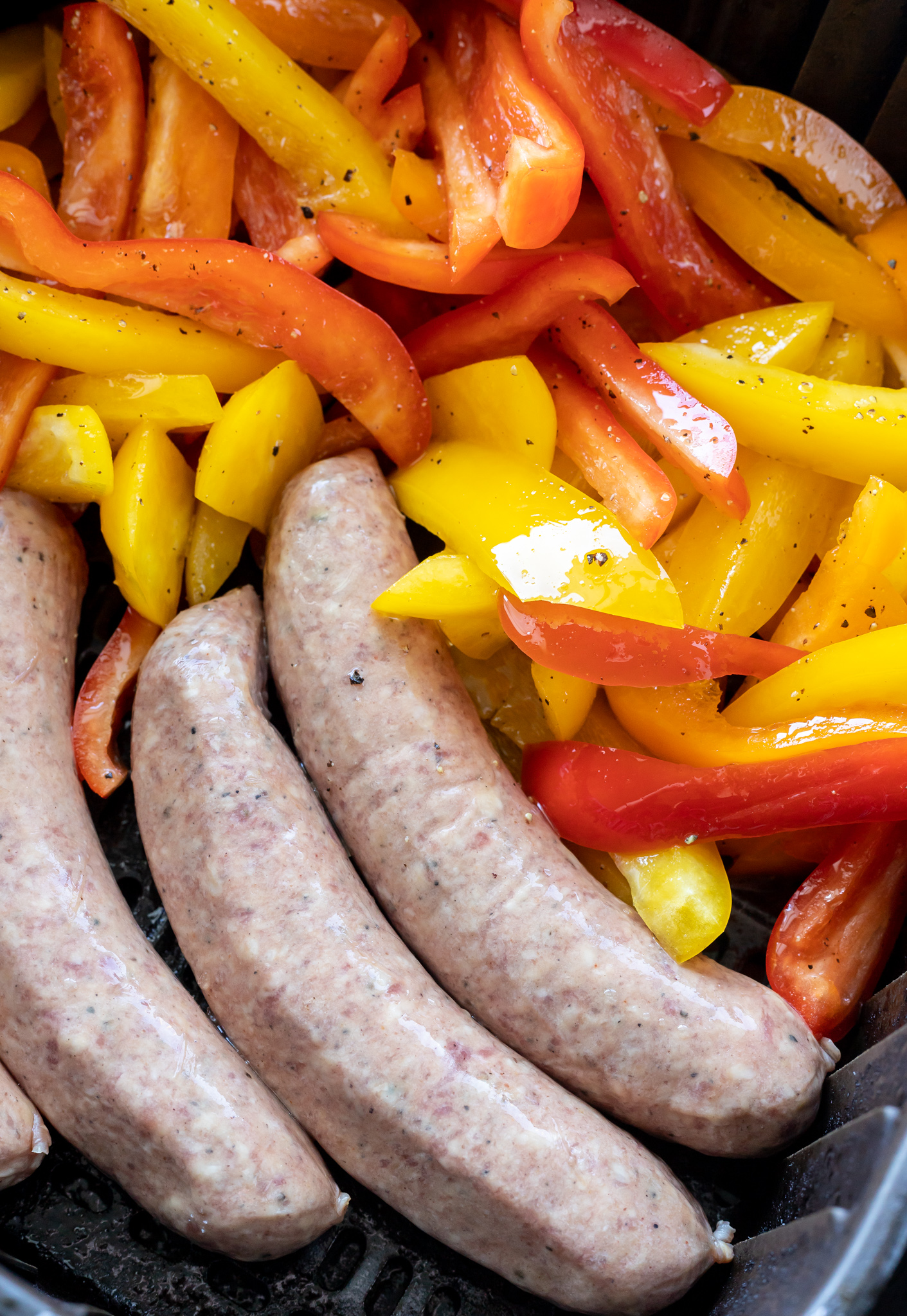 uncooked brats and sliced pepper sin air fryer basket